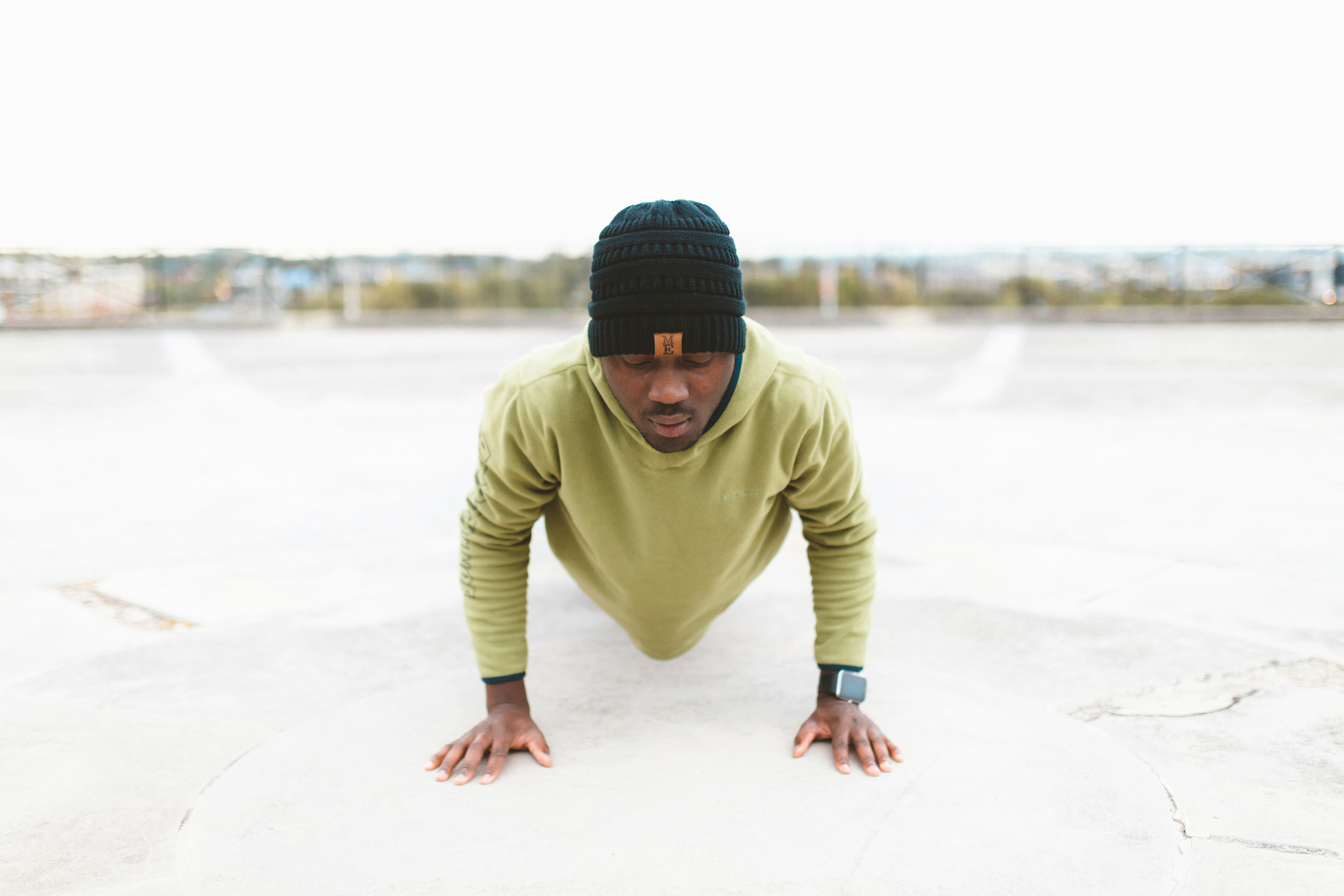 man in green long-sleeved shirt doing a push-up on gray concrete pavement